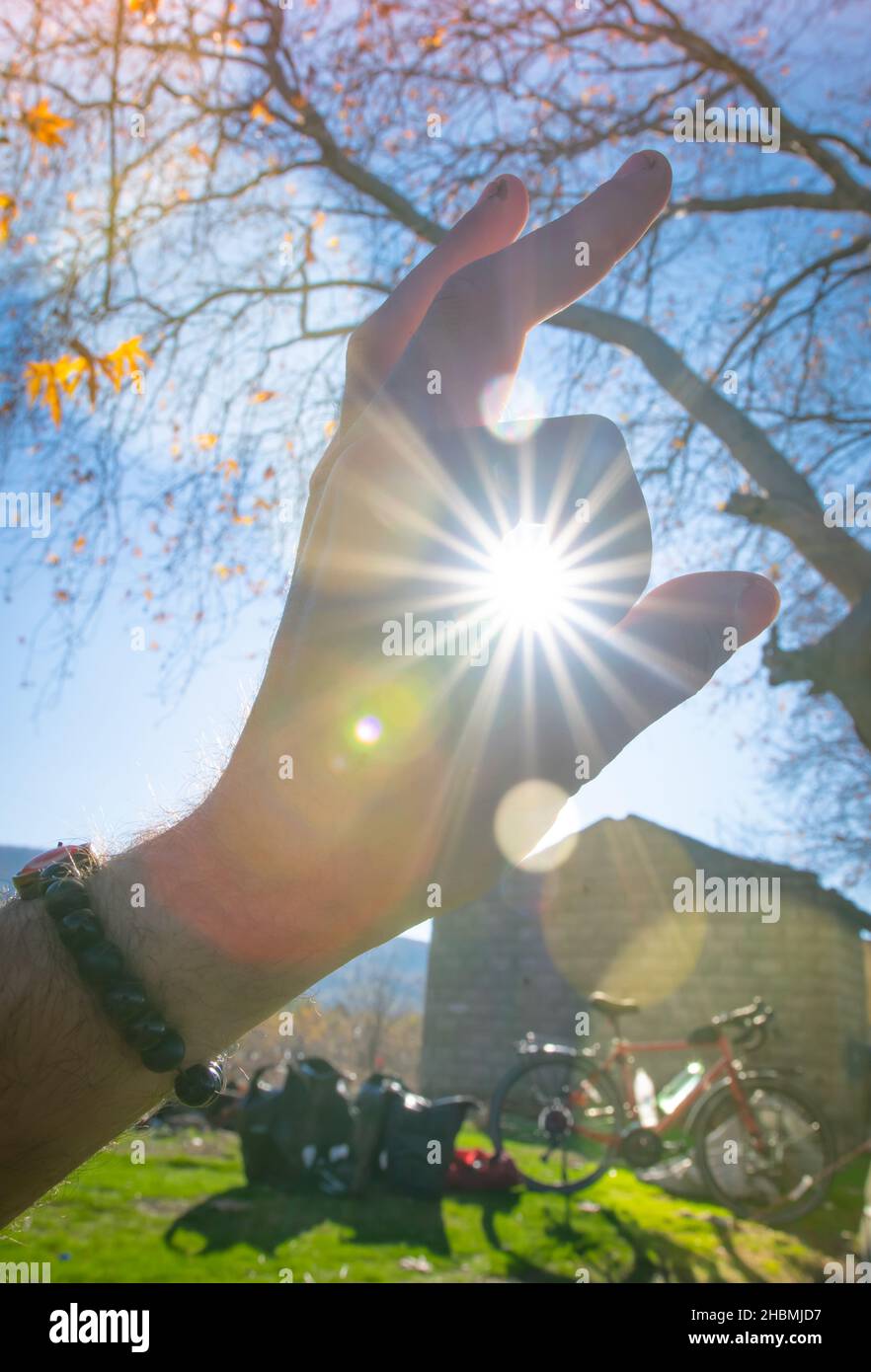 Hand fingers are covering Sunflare beams in autumn nature with bicycle and camping gear in the backgroun. Vintage bakground image of travel,  morning Stock Photo