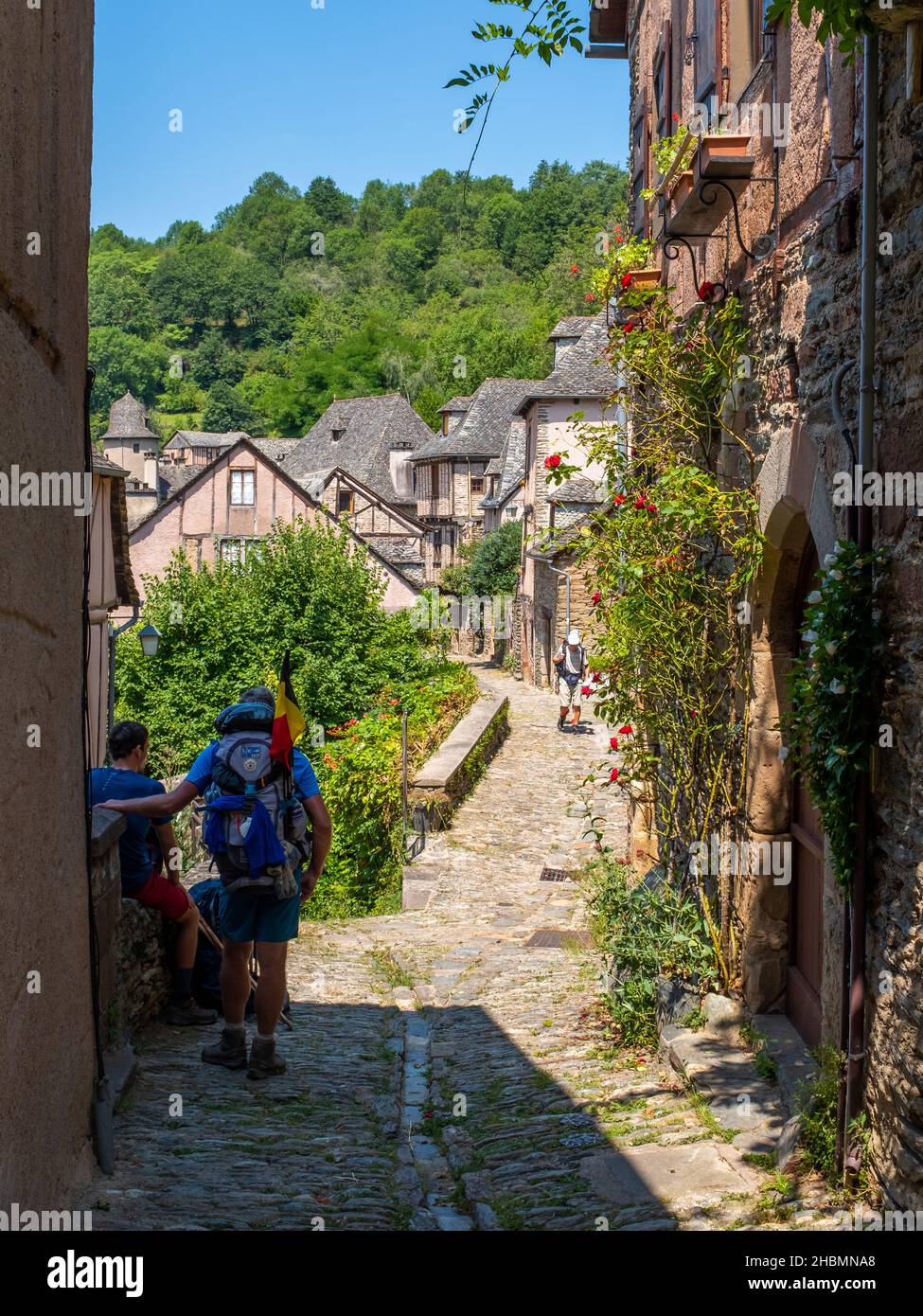 Conques, France - July 21, 2021: Three hikers on a cobblestone street of a medieval town, on the Way of St. James in France during a warm sunny summer Stock Photo