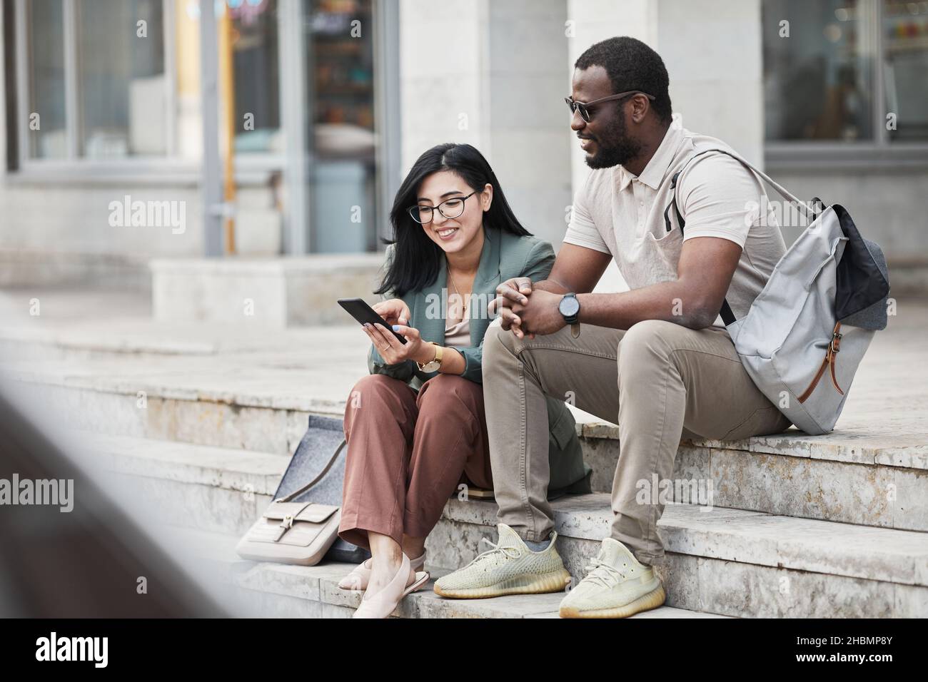 Portrait of two young business people chatting while sitting on steps in city, copy space Stock Photo