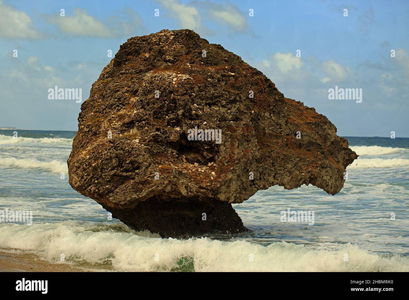 Large Boulder in Bethsheba, Barbados with splashing waves and a light blue sky. Stock Photo
