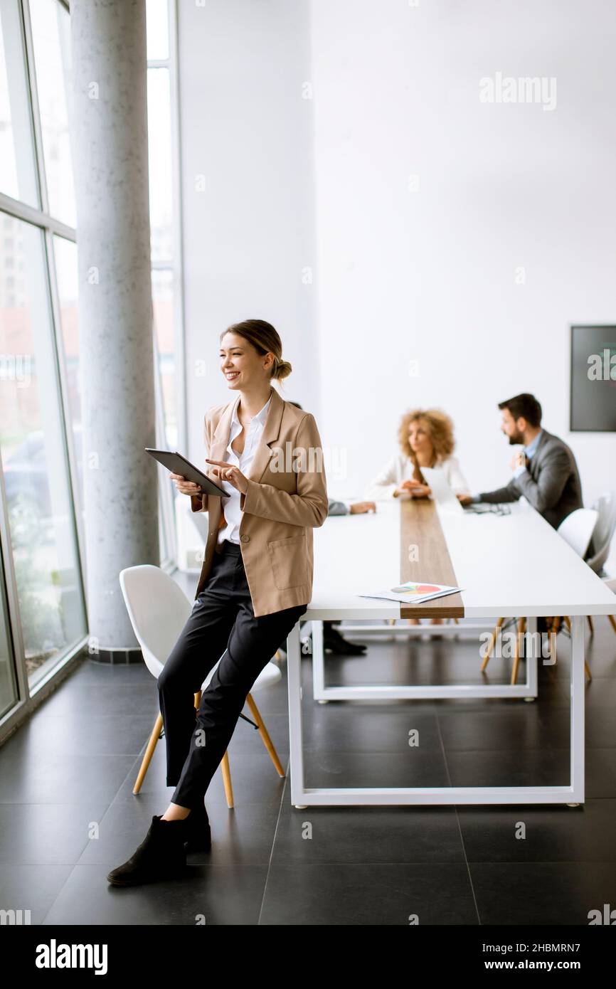 Young woman holding digital tablet and working in modern office in front of her team Stock Photo