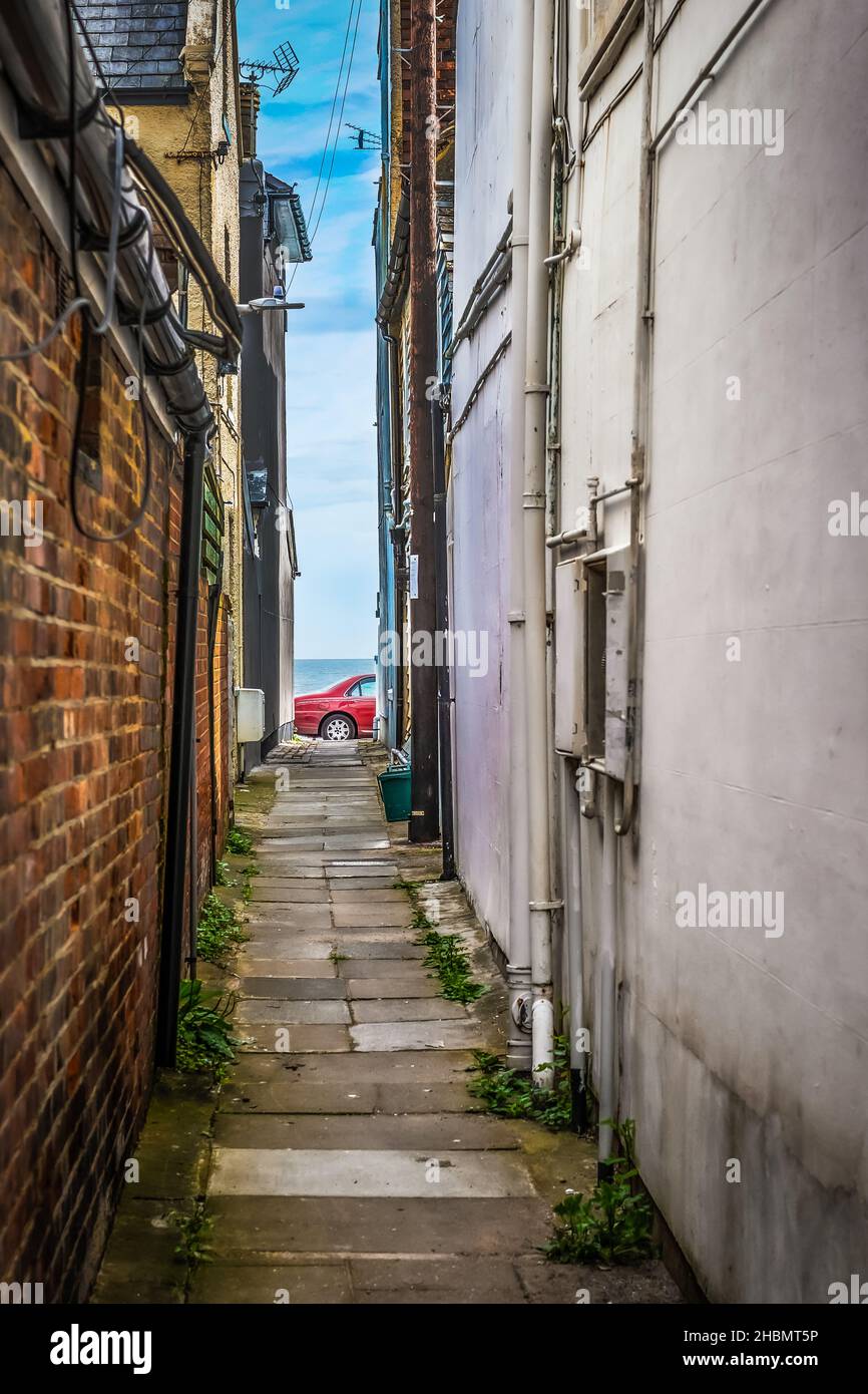 Looking down an empty narrow alleyway towards a red parked car and the sea in the background, taken at Sandgate near Folkestone 26th June 2021 Stock Photo