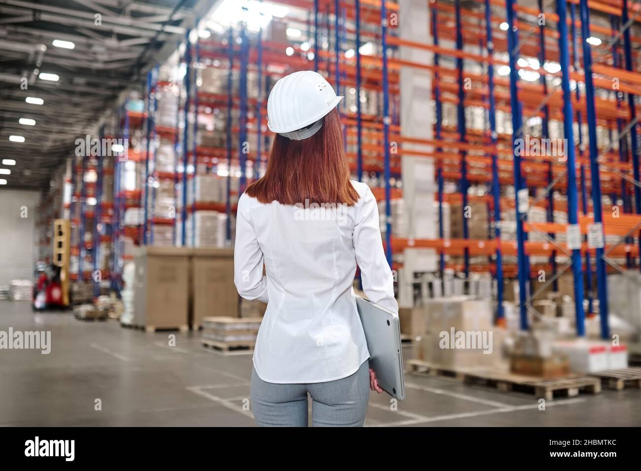 Woman with laptop in warehouse with back to camera Stock Photo