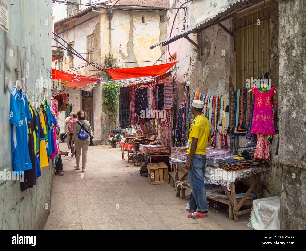 STONE TOWN, ZANZIBAR, TANZANIA - MARCH 13, 2017: Narrow Street with Tourists and Merchant Selling Colorful Fabrics in Stone Town, Zanzibar Stock Photo