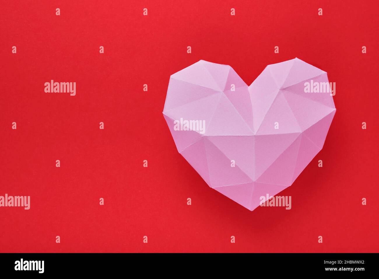 Pink paper heart isolated on red background. Red polygonal paper heart for Valentine's day or any other Love invitation cards. Top view, copy space. Stock Photo