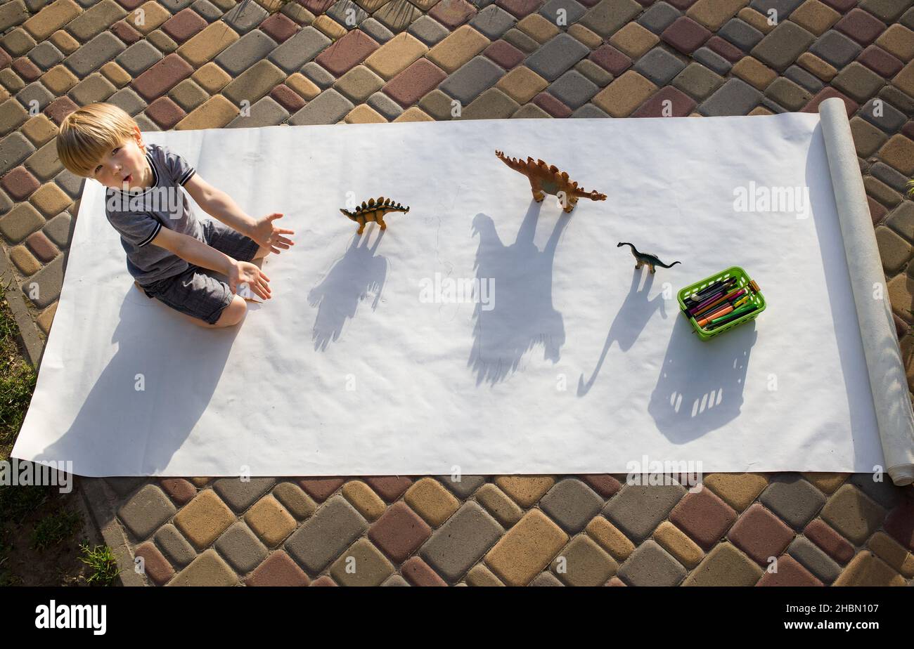 child plays with figures of dinosaurs and their shadows, draws contrasting shadows from them . creative ideas for children's creativity. Fun activitie Stock Photo