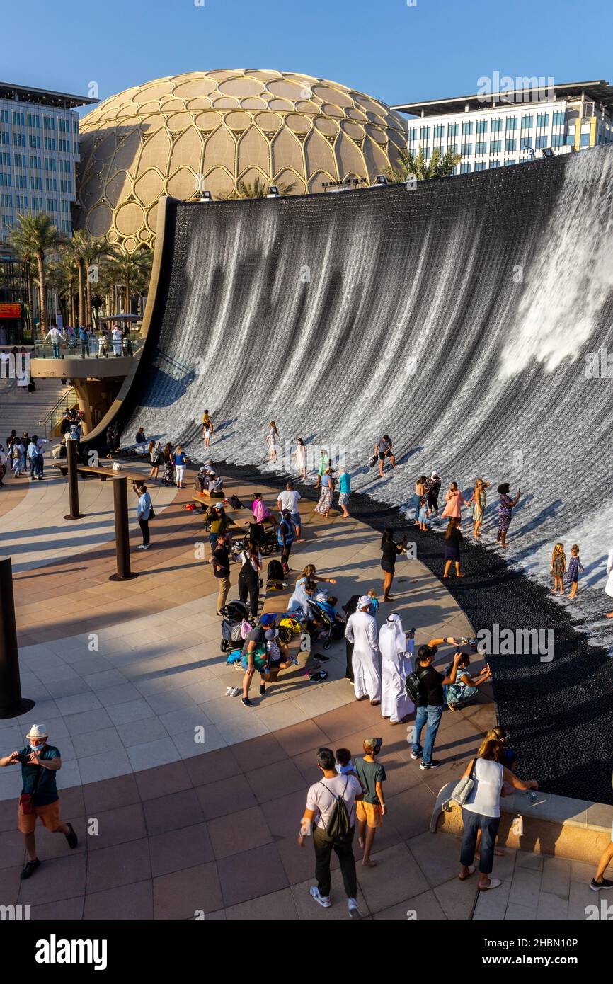 Dubai, UAE, 09.12.2021. Expo 2020 Dubai Water Feature, monumental fountain in Jubilee Park with people playing in the water and Al Wasl Plaza dome. Stock Photo