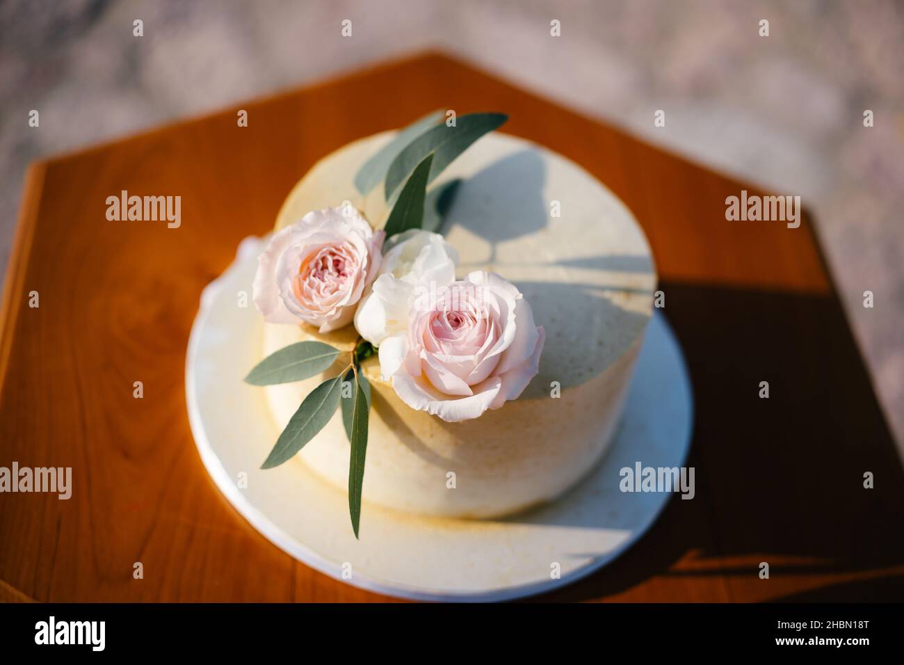 White wedding cake with roses and green leaves, stands on a wooden table. Top view Stock Photo