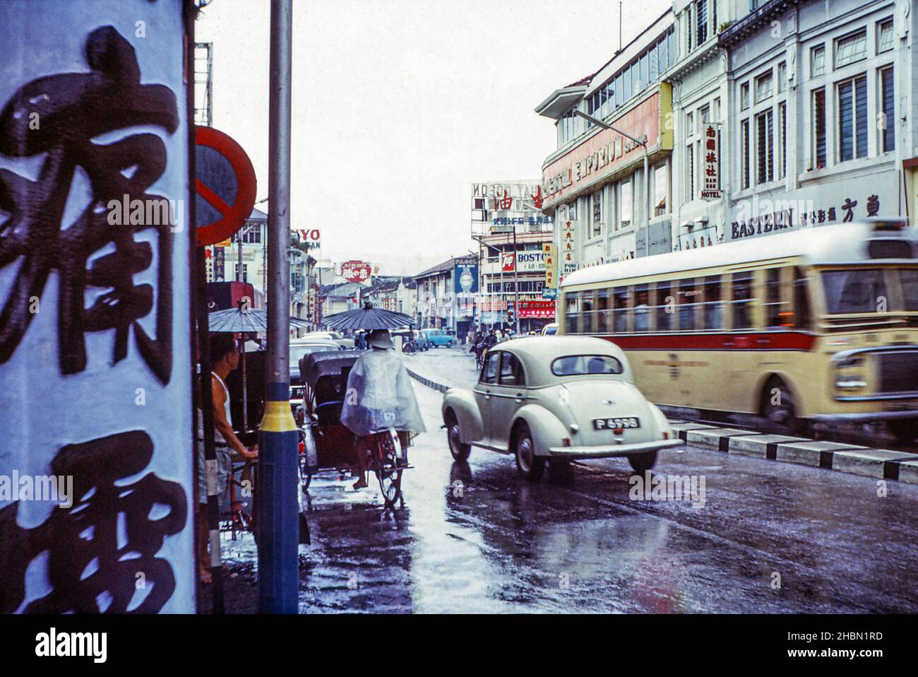 Penang Road, Georgetown, Penang, Malaysia, including The Oriental Emporium, right of centre. Also has a car passing a trishaw, in the rain. 1970 Stock Photo