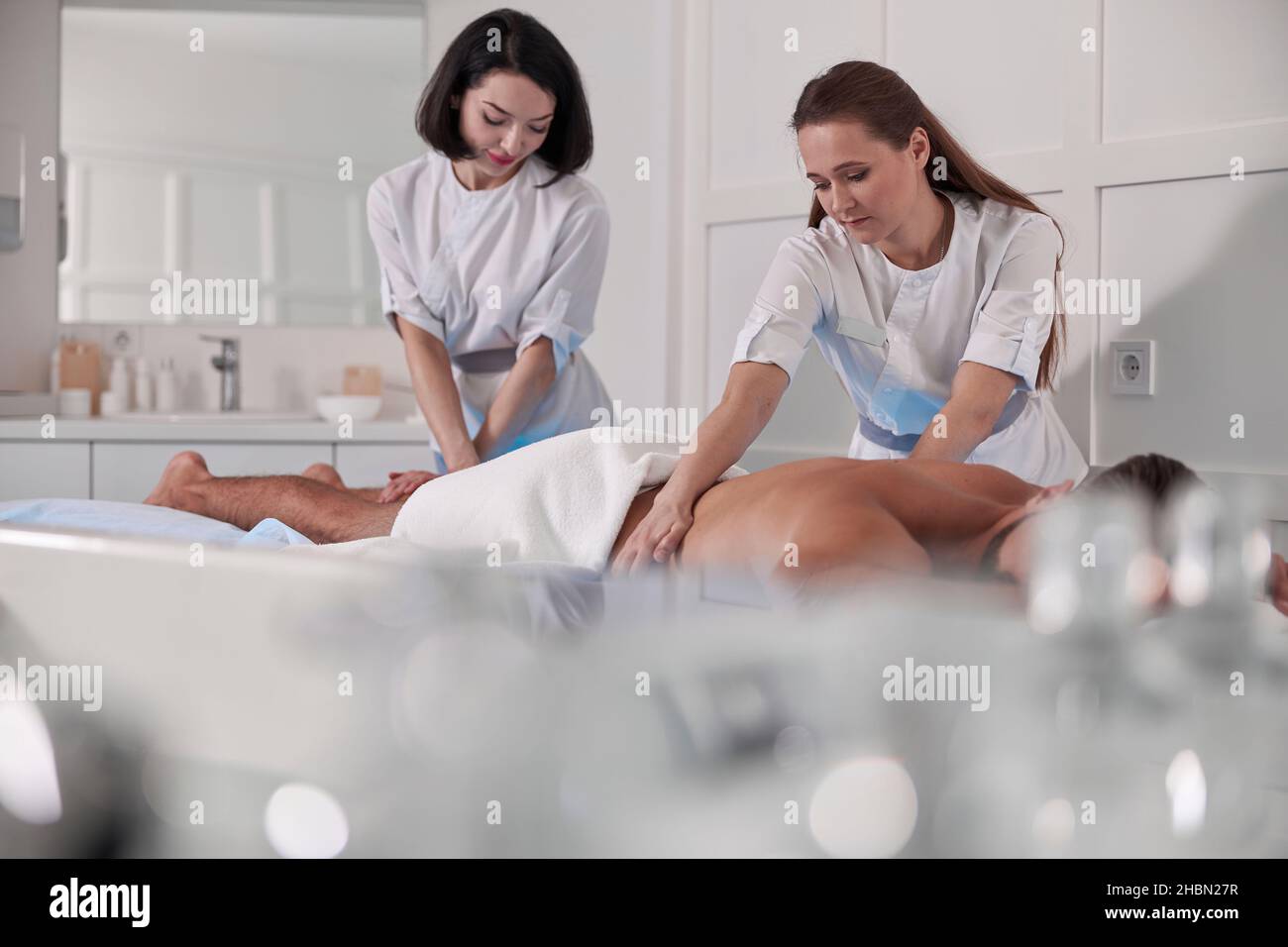 Therapists do massage of back and legs to male client in contemporary hospital office Stock Photo