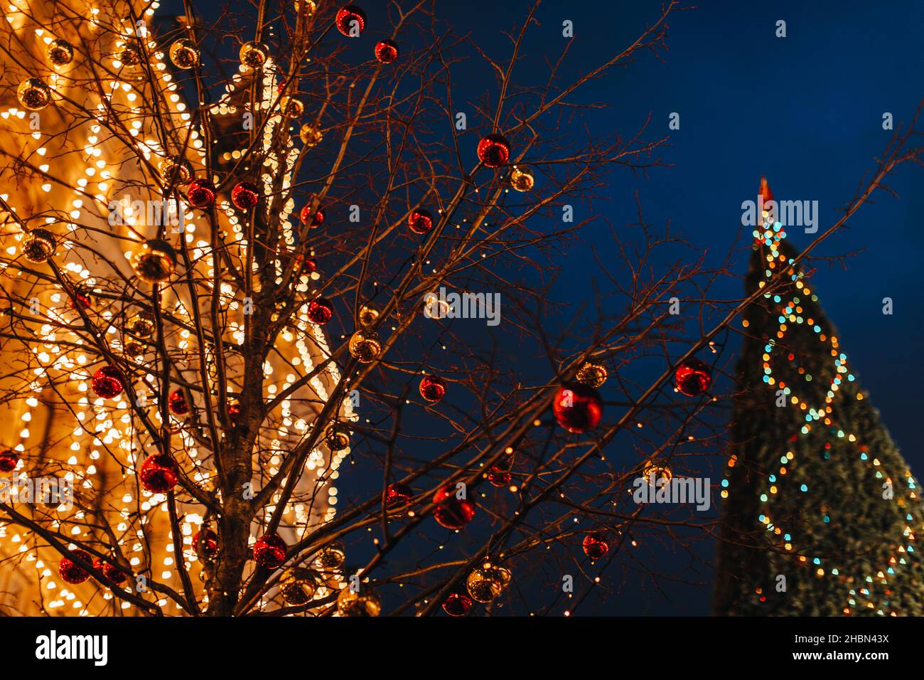 Golden vintage building and Christmas tree branches decorated with Christmas balls in festive evening magic atmosphere. GUM exterior, Moscow center Stock Photo