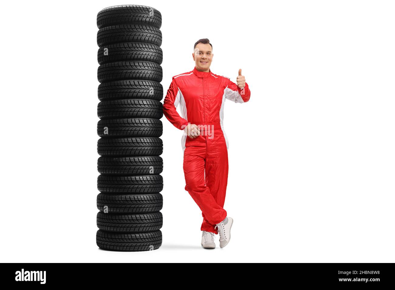 Full length portrait of a racer leaning on a pile of tires and gesturing a thumb up sign isolated on white background Stock Photo
