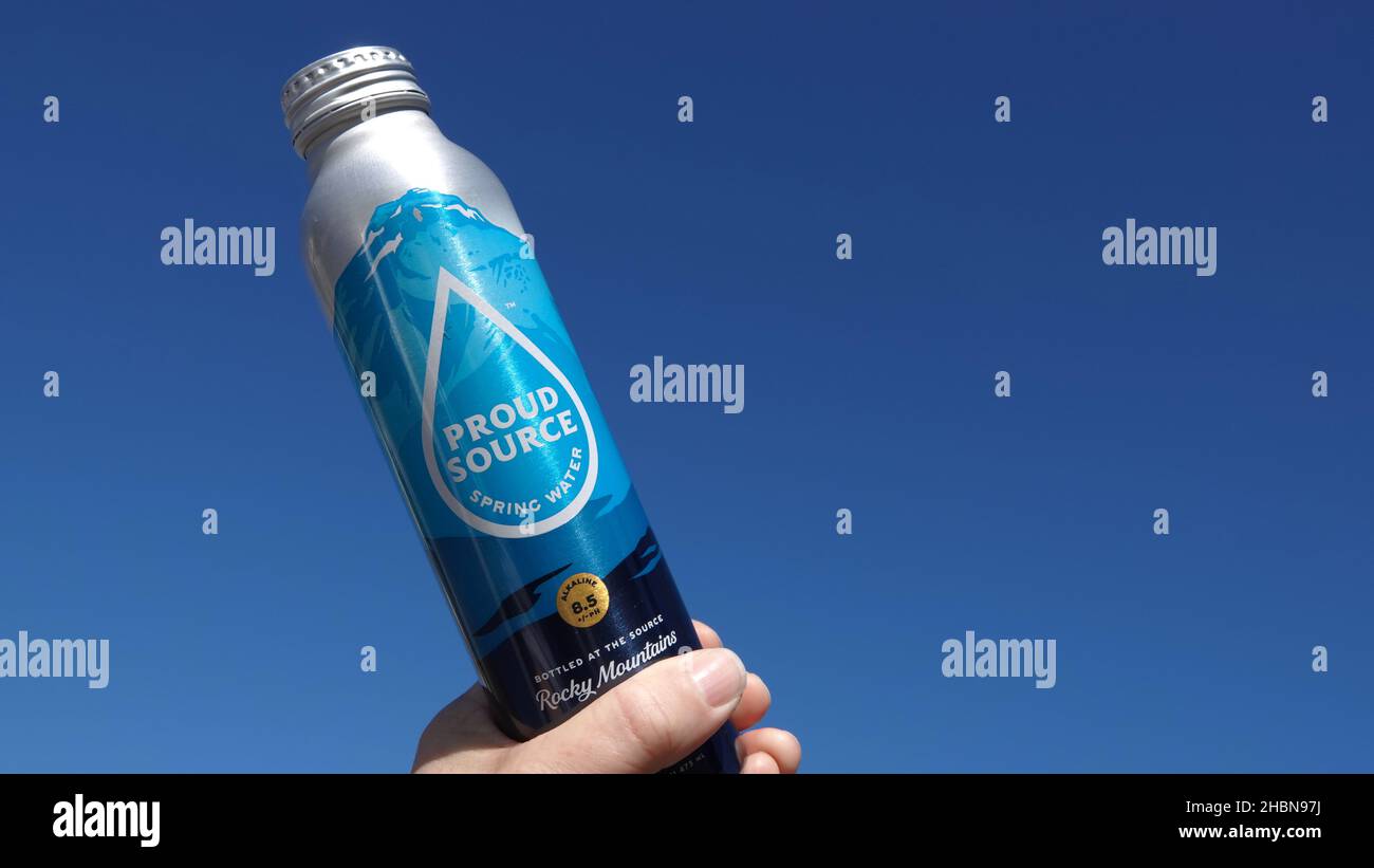 Close up of a hand holding up a Proud Source water bottle against blue sky. Illustrative editorial Stock Photo