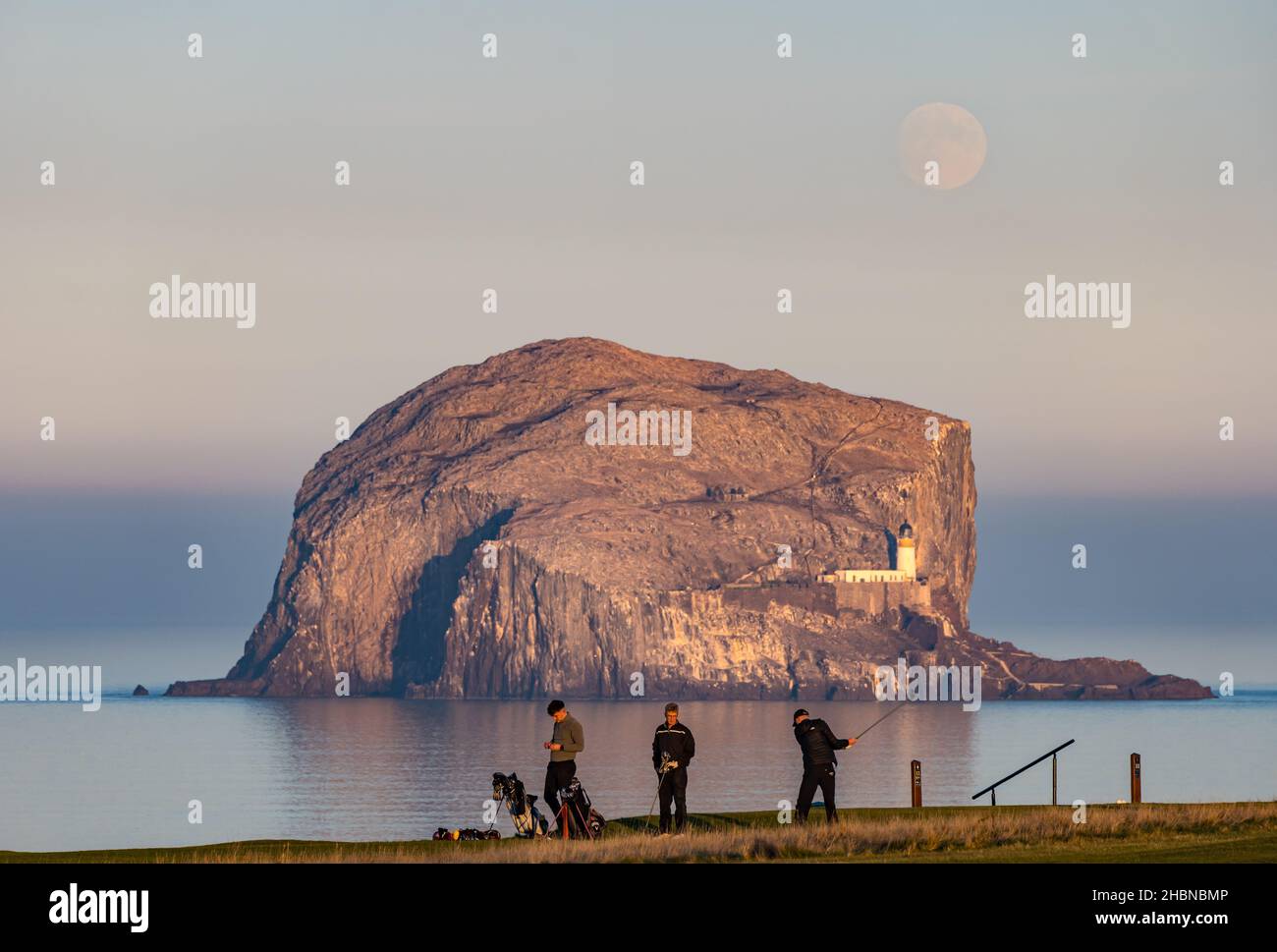Men playing golf at dusk on Glen golf course, North Berwick in front of Bass Rock, Firth of Forth, Scotland, UK Stock Photo