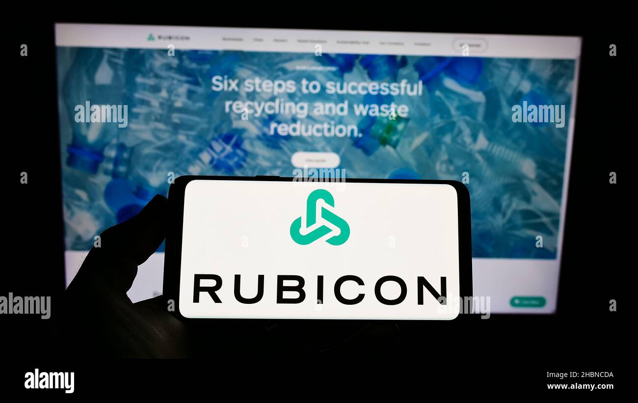 Person holding smartphone with logo of US software company Rubicon Technologies LLC on screen in front of website. Focus on phone display. Stock Photo