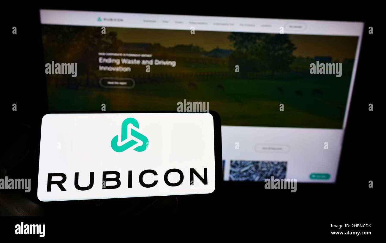 Person holding mobile phone with logo of American software company Rubicon Technologies LLC on screen in front of web page. Focus on phone display. Stock Photo