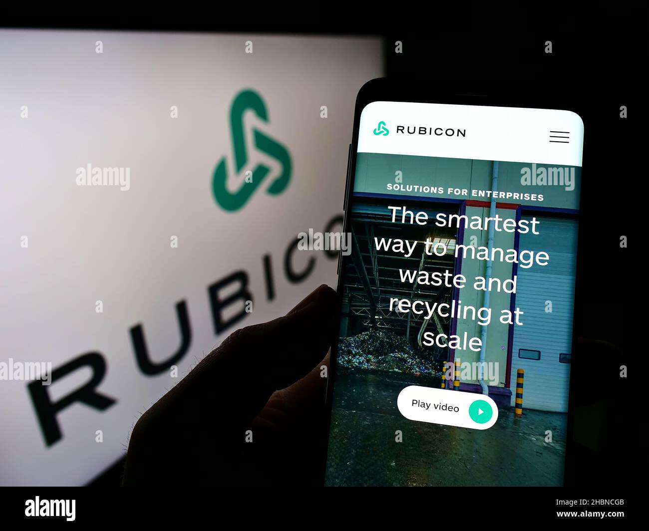 Person holding cellphone with website of US software company Rubicon Technologies LLC on screen in front of logo. Focus on center of phone display. Stock Photo
