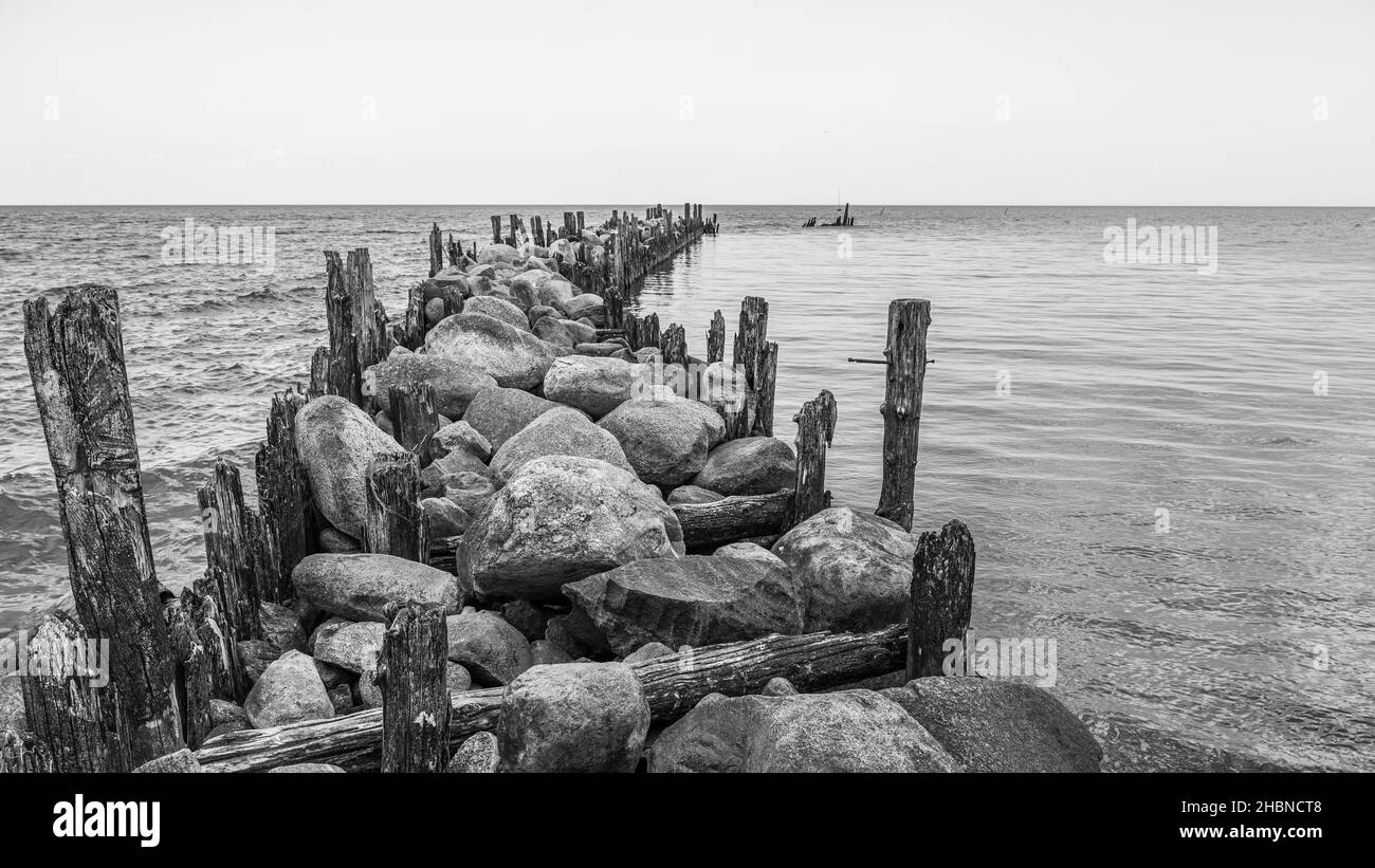 an old pier made of stones and wooden legs is left with metal screeds and the water surface is calm Stock Photo