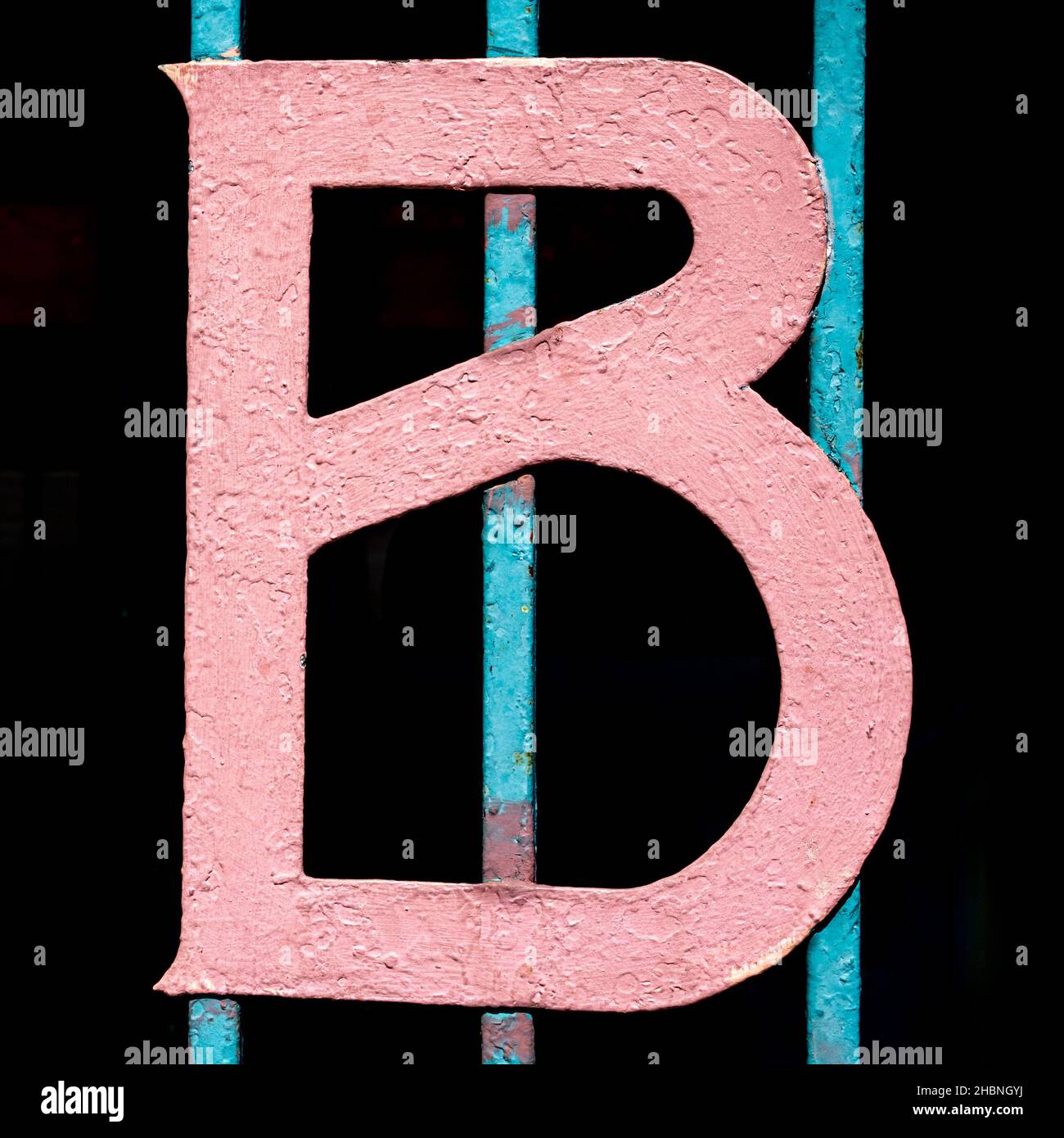 painted pink capital letter B on a blue fence with dark background Stock Photo