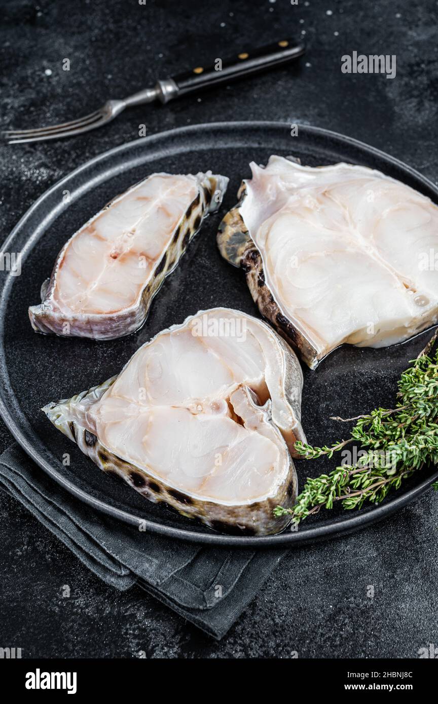 Wolf Fish Fillets Fresh Raw wolffish o wolf fish Steak on a plate. Black background. Top ...