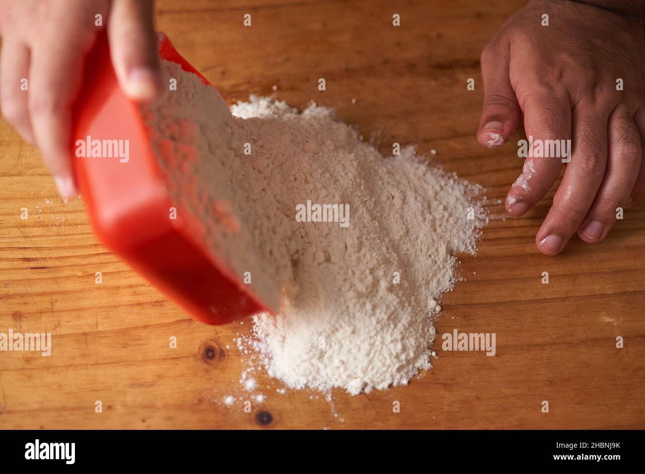 man empties portion of flour on wooden table Stock Photo