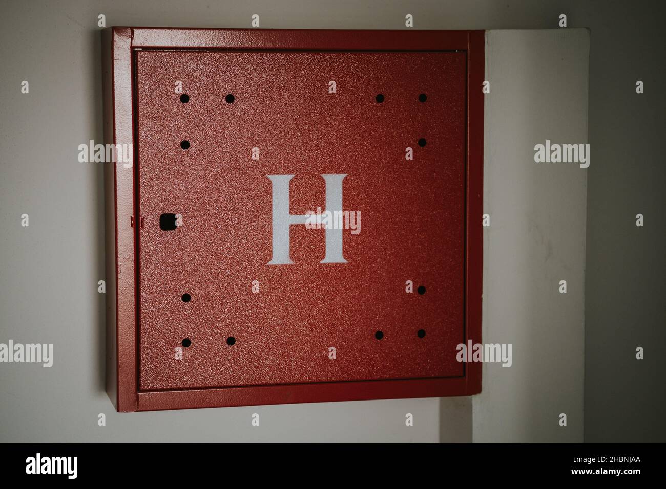 A closeup shot of a metal box with the letter H on the wall Stock Photo