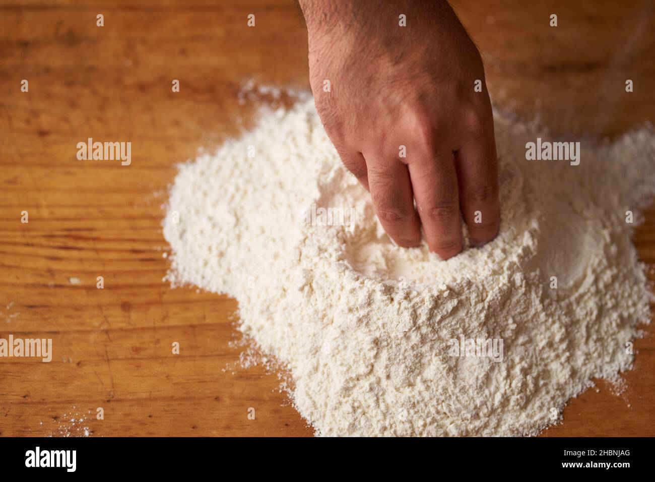 a cook's hands make a flour volcano on a wooden table Stock Photo