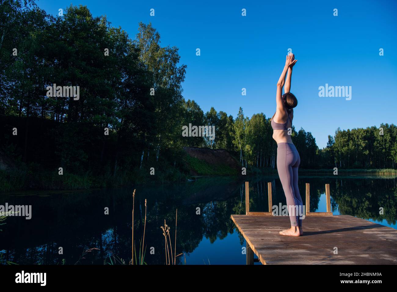 Young female practicing yoga against the sky on a sunrise. Pretty slim woman performs an exercise. Healthcare, meditaion, welness, mindfulness concept Stock Photo