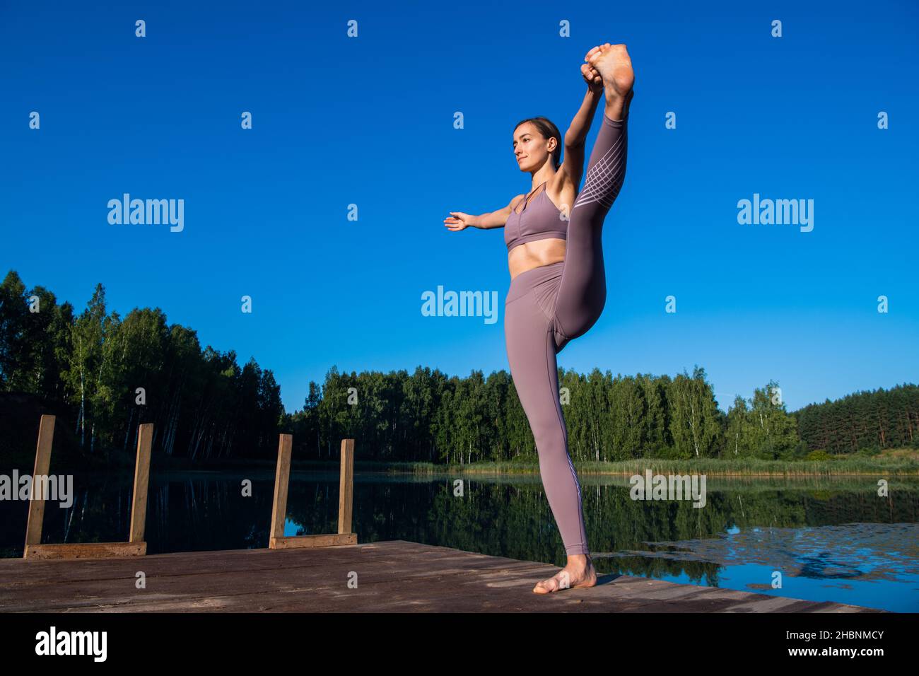 Young female practicing yoga against the sky on a sunrise. Pretty slim woman performs an exercise. Healthcare, meditaion, welness, mindfulness concept Stock Photo
