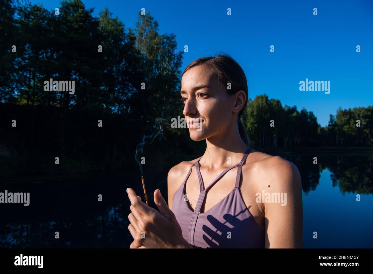 Young female practicing yoga against the sky on a sunrise. Pretty slim woman performs an exercise. Healthcare, meditaion, welness, mindfulness concept Stock Photo