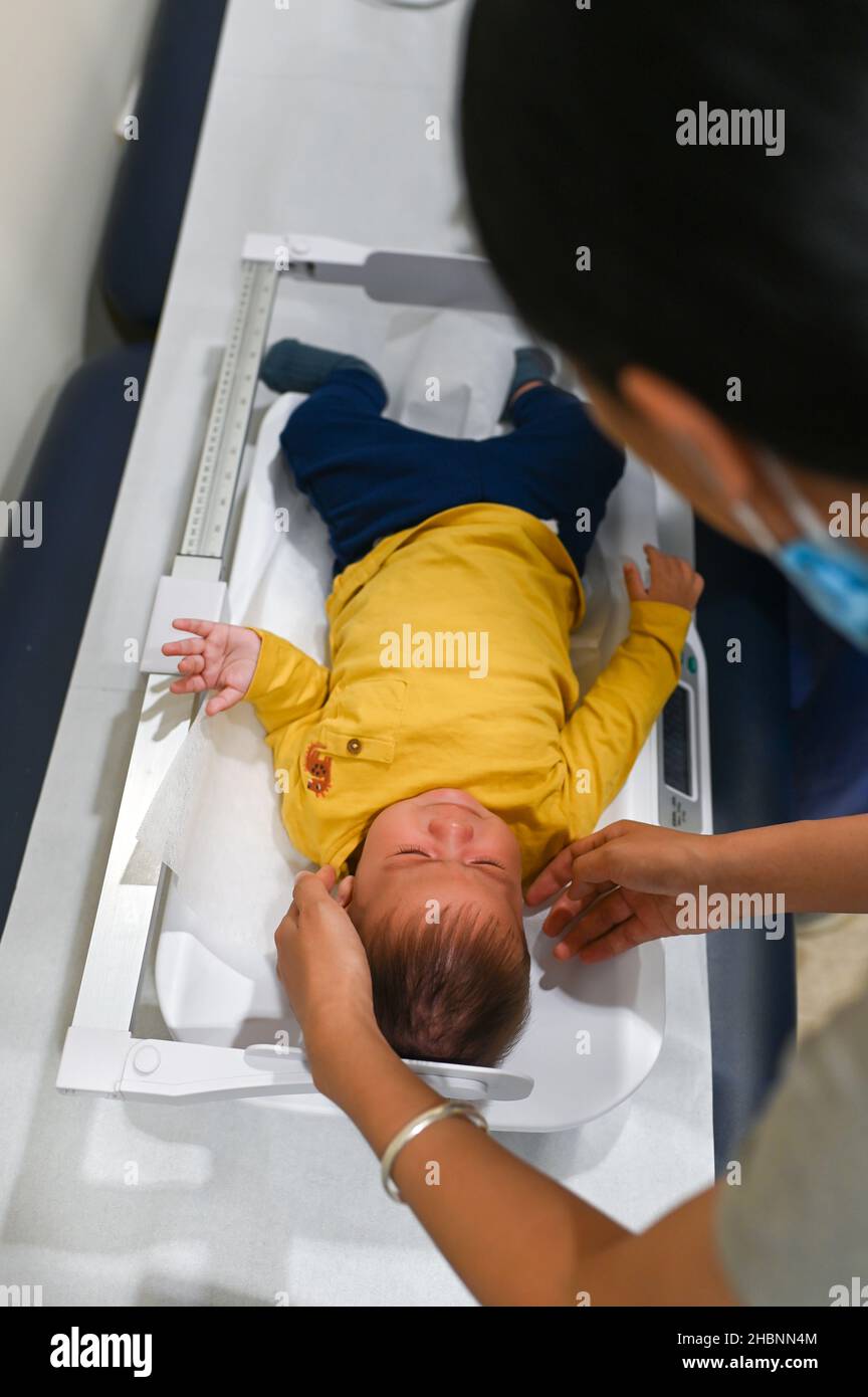 Doctor measuring length and weight of a 5 months old mixed race baby boy at the doctors office for a routine checkup and physical exam to track progre Stock Photo