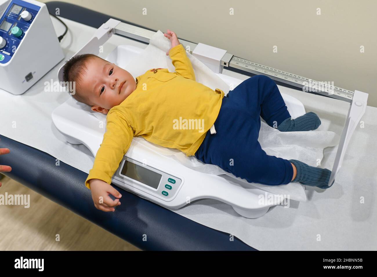 5 months old mixed race baby boy on a weighting scale at the doctors office for a routine checkup and physical exam to track progress at the hospital Stock Photo
