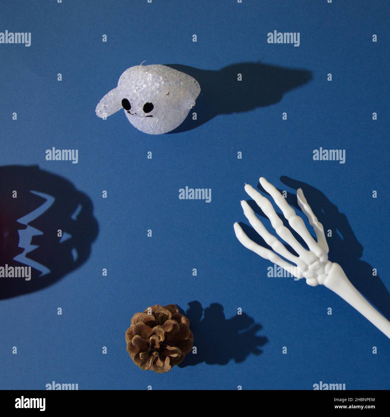 A ghost, pine cone, and hand skeleton with shadows, with a shadow of Halloween pumpkin Stock Photo