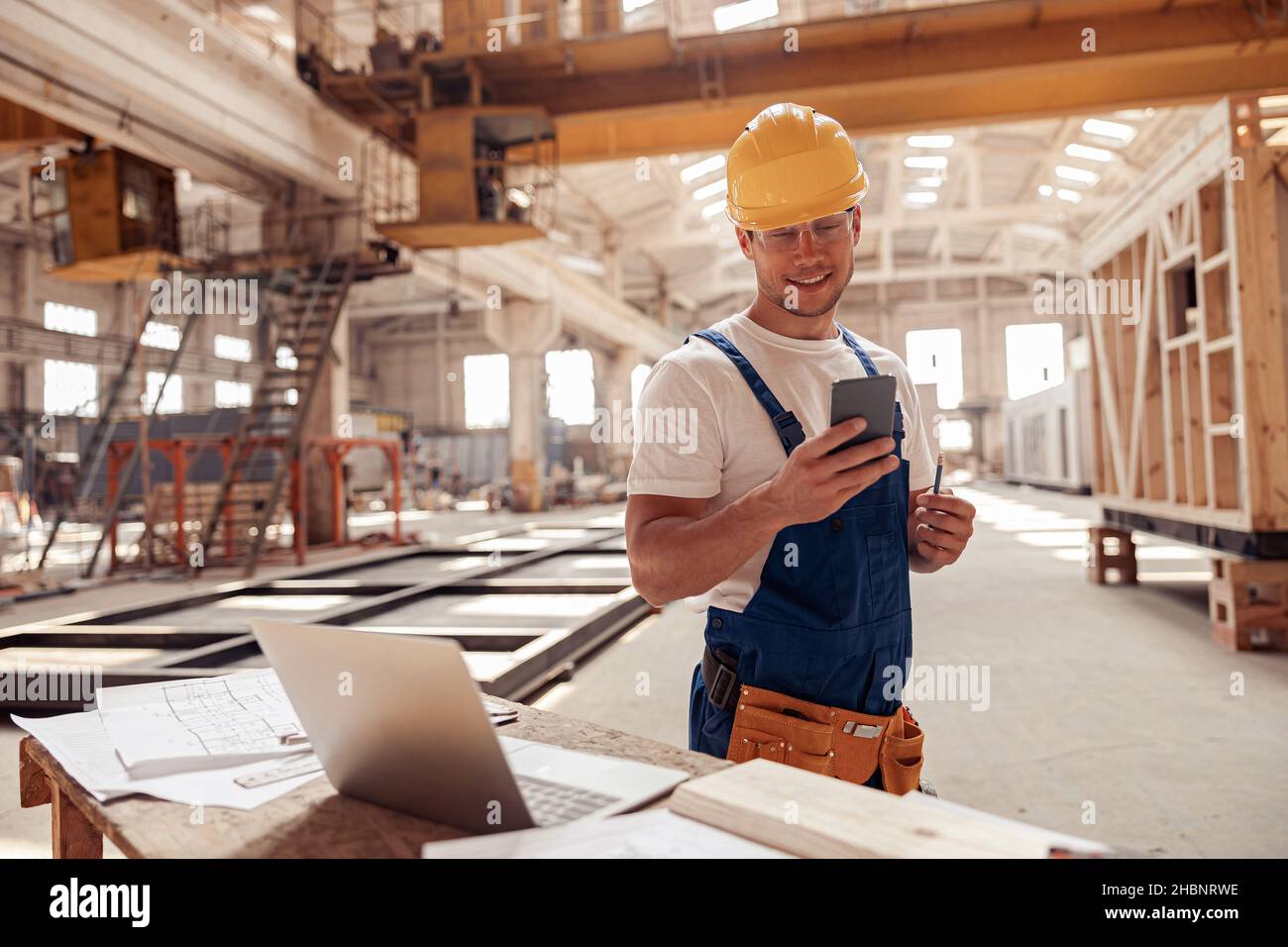 Cheerful builder using smartphone at construction site Stock Photo