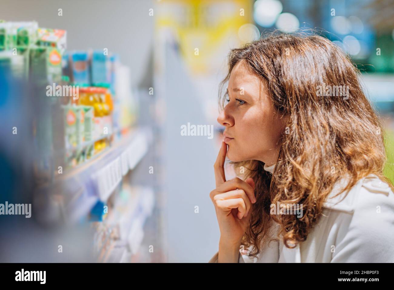 young woman mother reads the composition of children's food, examines the ingredients on juices in the supermarket, a portrait of an attentive shopper Stock Photo