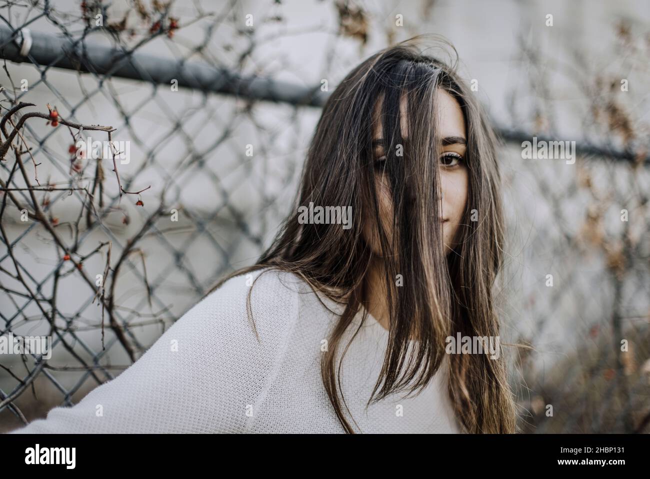 portrait of teenage girl with hair in face against chain link fence Stock Photo