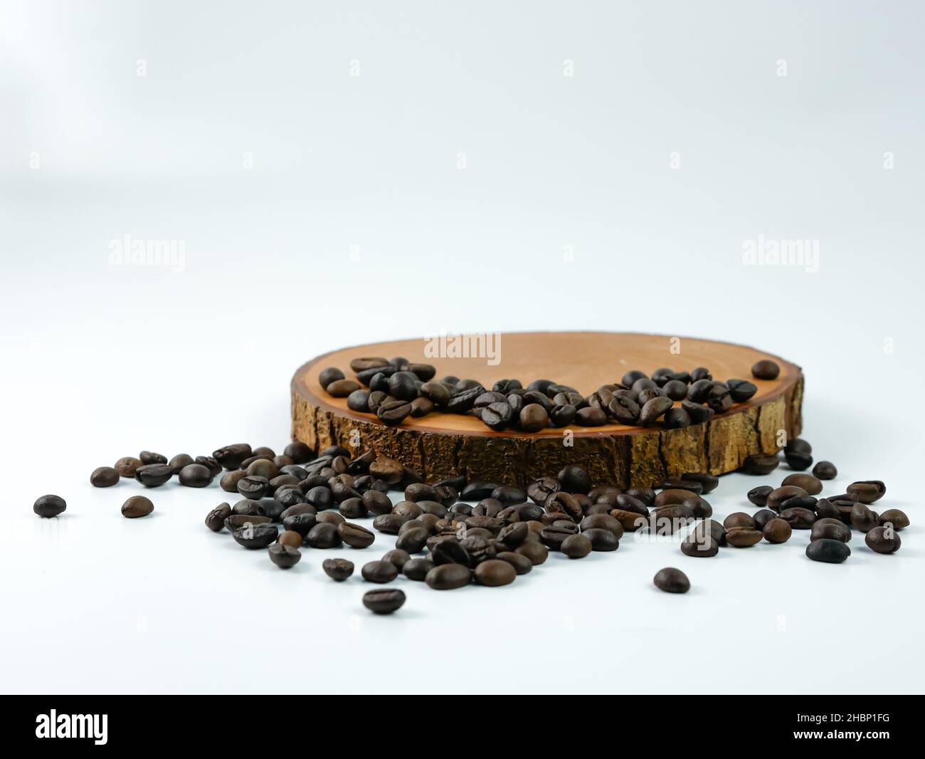 Coffee beans scattered on a round wooden plank isolated on a white background. Product placement concept. Stock Photo