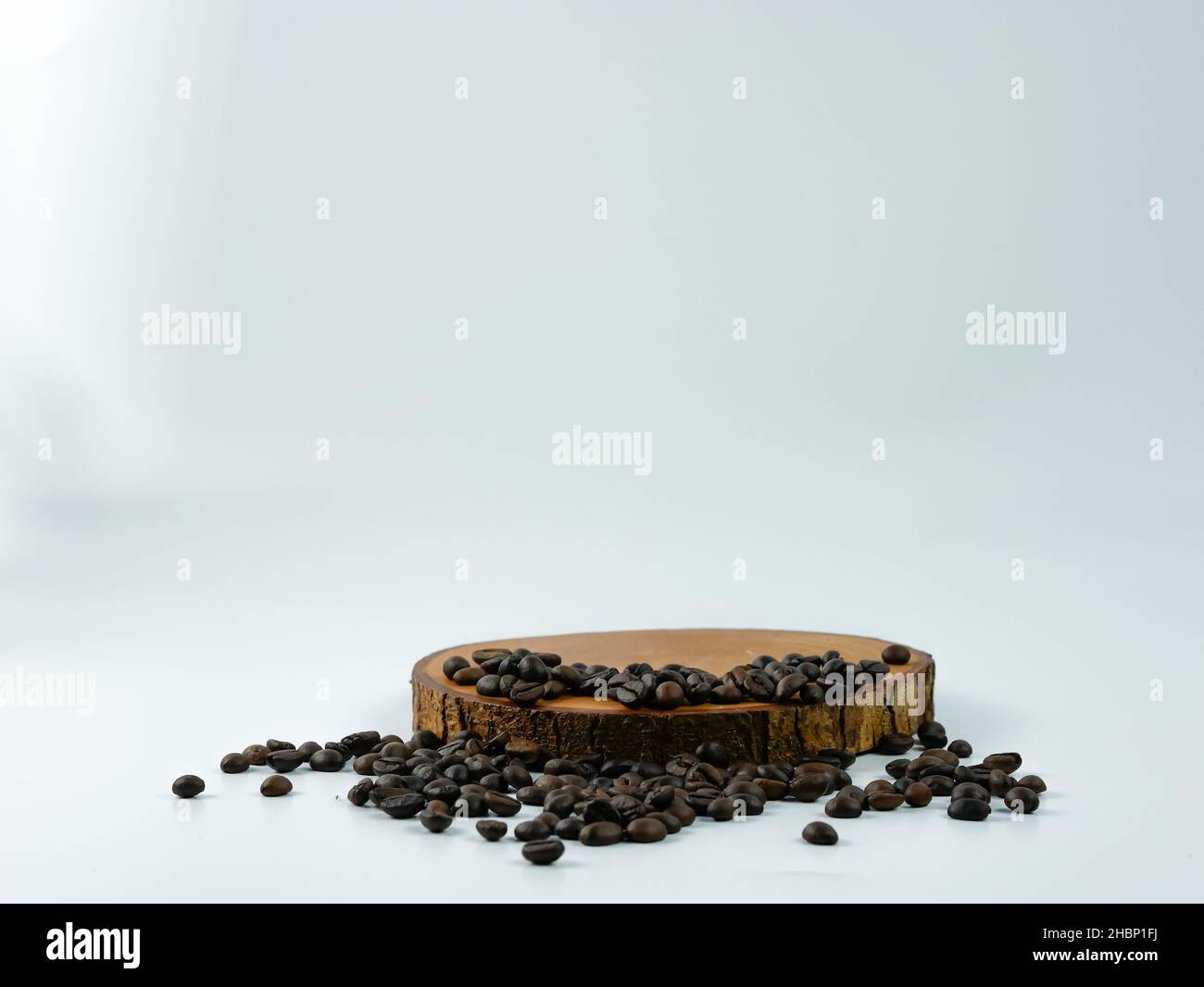 Coffee beans scattered on a round wooden plank isolated on a white background. Product placement concept. Stock Photo