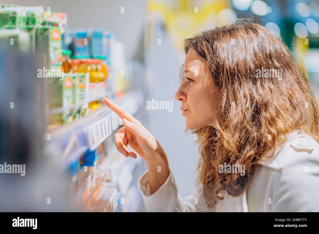 attentive young woman reads the composition on baby juice in the supermarket, looks at the ingredients on the packaging Stock Photo