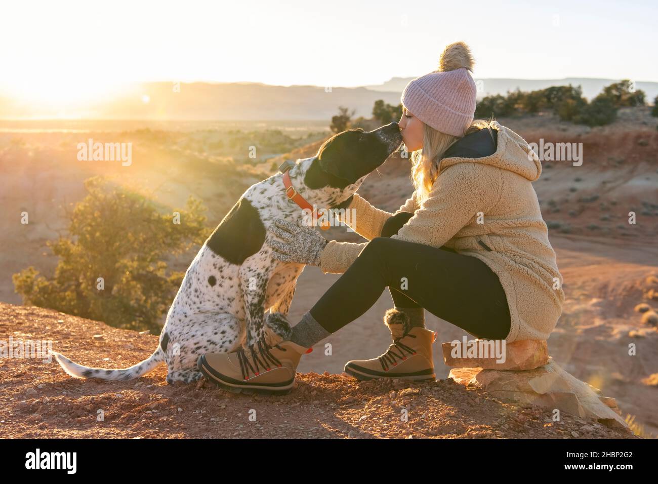 Female hiker kissing dog while in the desert during sunset Stock Photo