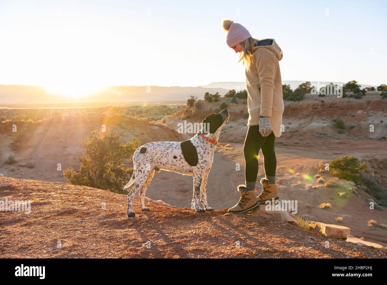 female hiker looking at dog while standing in desert during sunset Stock Photo