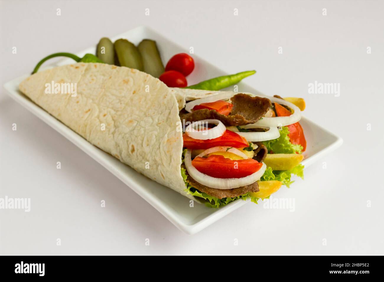 Traditional Turkish kebab,doner wrapped with flat bread,lavas and tomato,lettuce,onion rings and fried potatoes on long plate Stock Photo