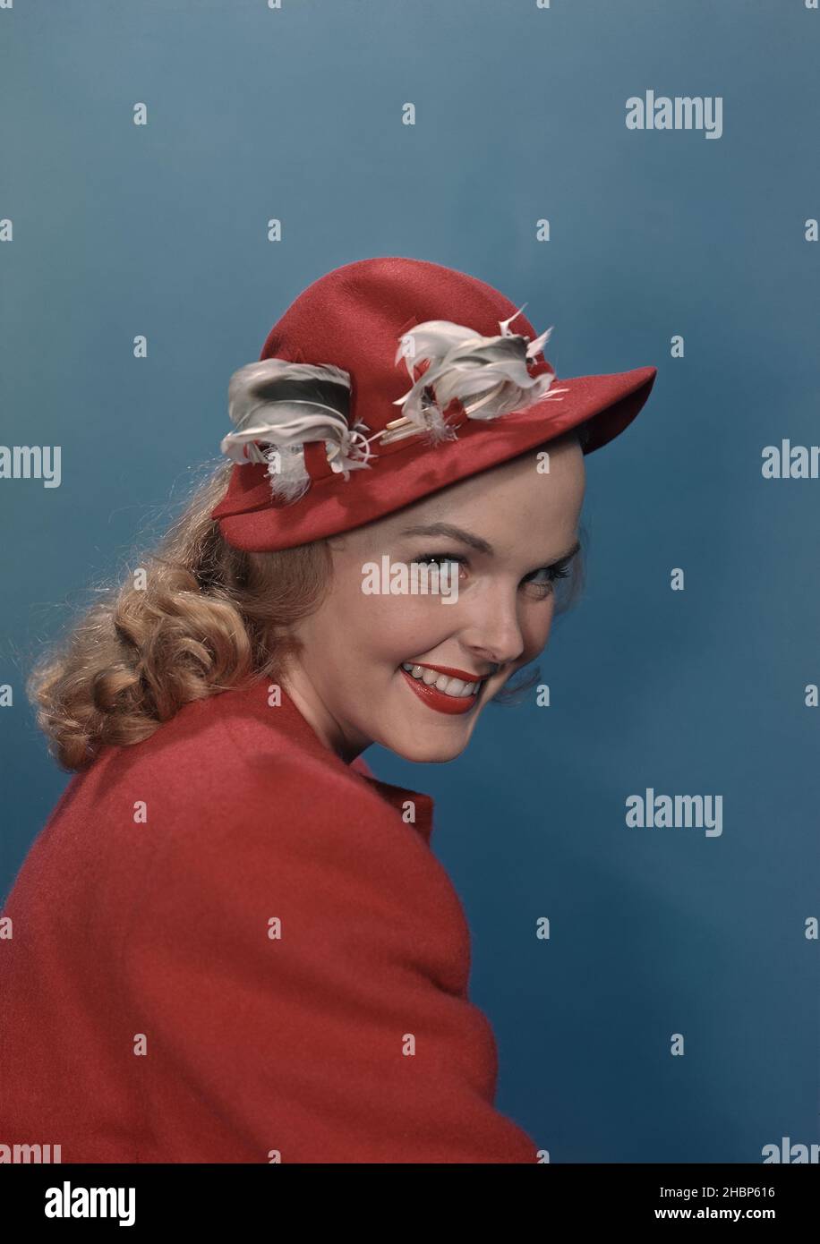 Portrait of young woman in red coat and hat sitting sideways Stock Photo