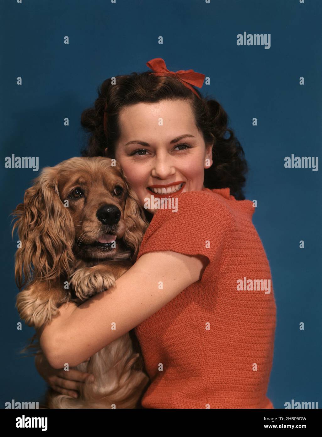 Dark haired teen in red sweater with red ribbons in her hair, loving her brown cocker spaniel puppy Stock Photo