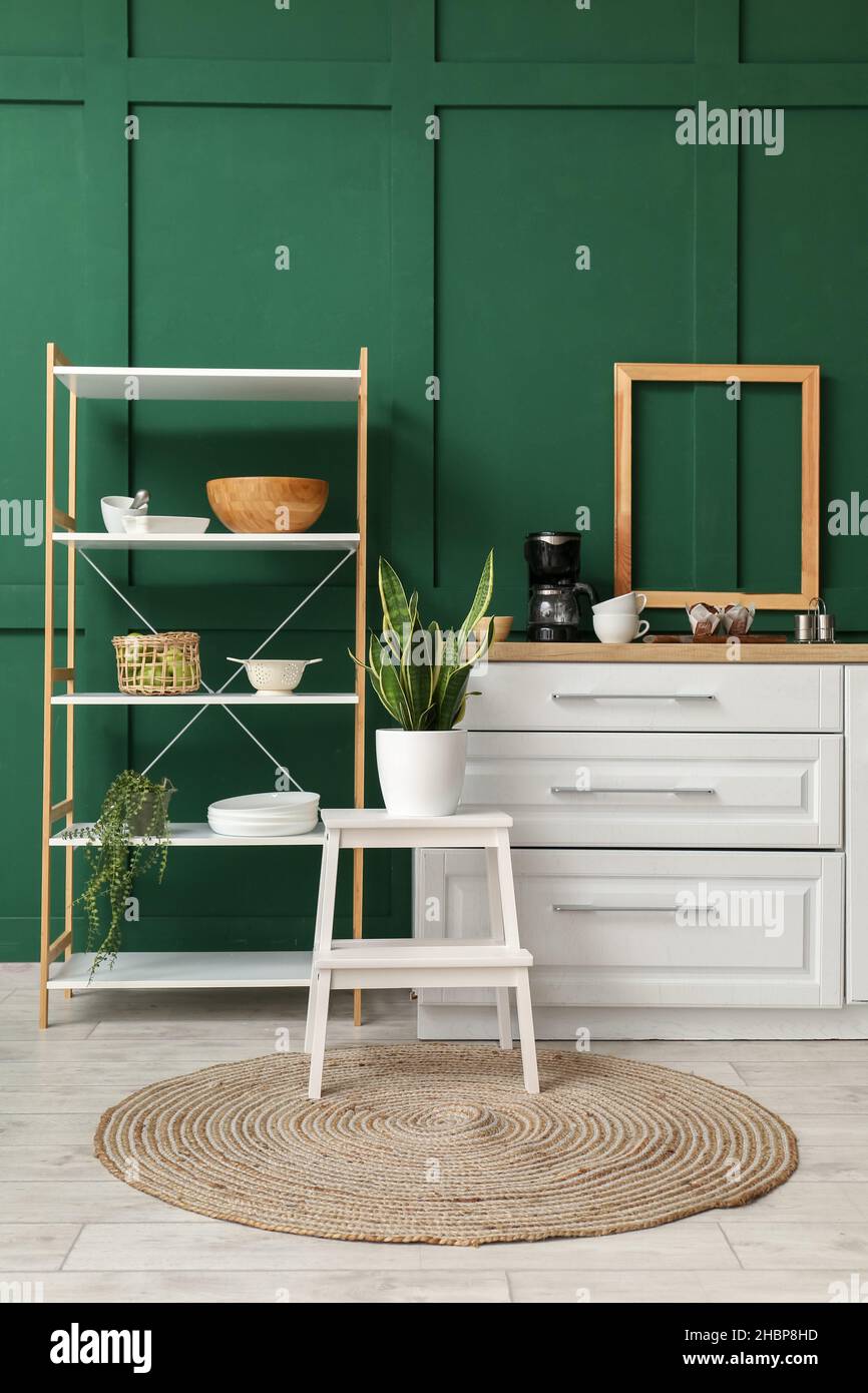 Interior of stylish kitchen with white counter, shelving unit and green