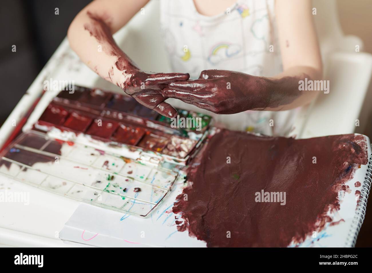 Child play mess with paint making big stain on paper and hands Stock Photo