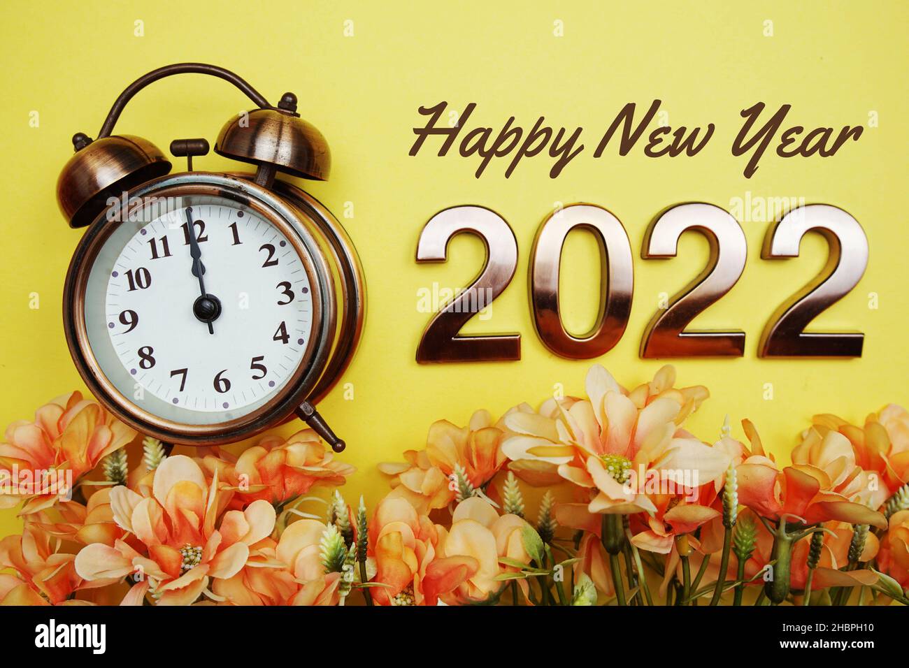Happy New Year 2022 text with alarmclock and flower decoration on yellow background Stock Photo