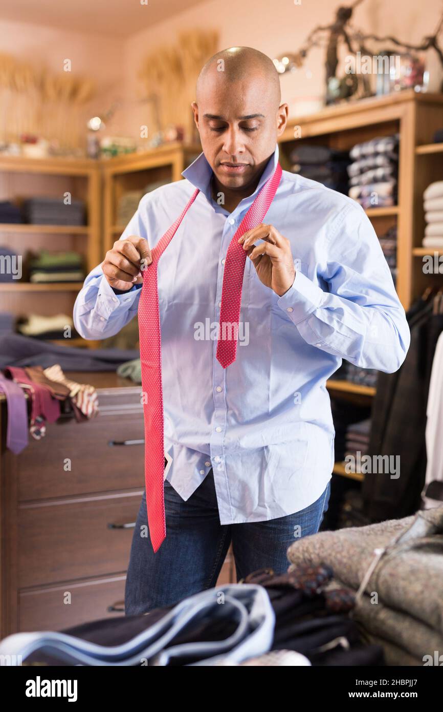 Positive young adult man choosing tie in clothing store Stock Photo - Alamy