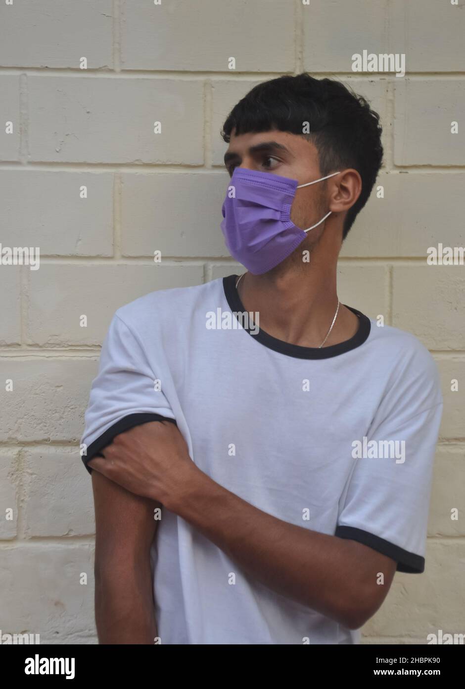 Front view of a young guy wearing face mask with looking sideways while posing against white wall Stock Photo