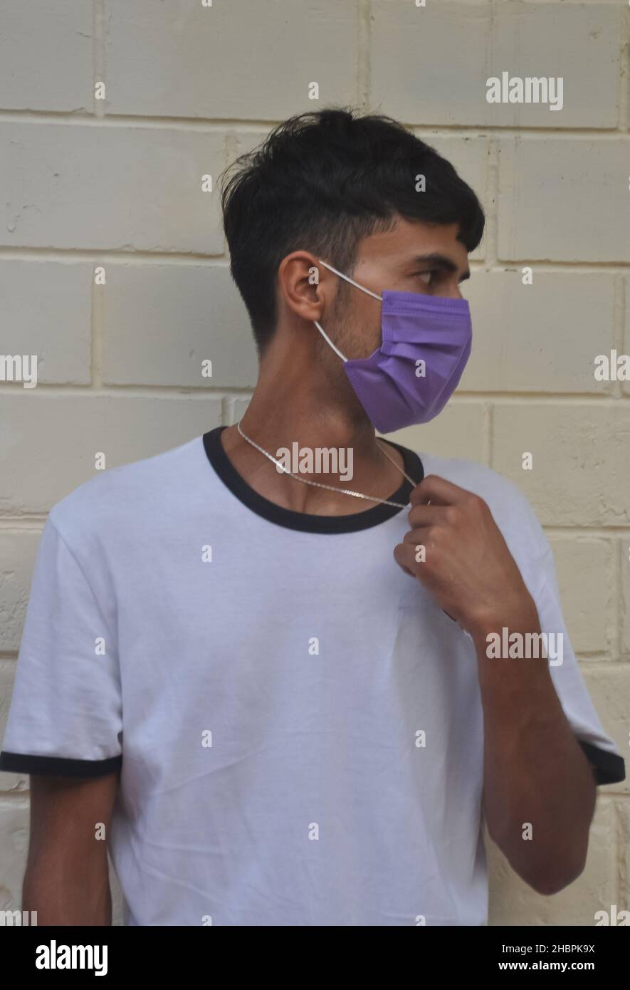 Front view of a young guy wearing face mask with looking sideways while posing against white wall Stock Photo